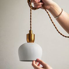 a hand holding a white and gold colored light fixture with rope attached to the bulb