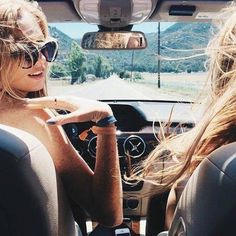 two women sitting in the back seat of a car, one with sunglasses on her head