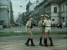 two women in uniforms talking to each other on the street with buildings in the background