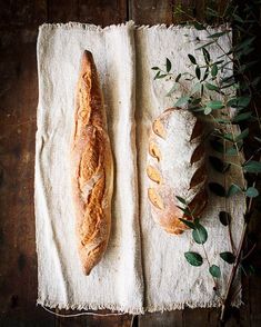 two loaves of bread sitting on top of a white towel next to green leaves