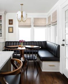 a kitchen with white cabinets and black leather banquet table set up next to a window