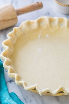 an uncooked pie crust sits on a marble counter top next to a rolling pin