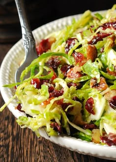 a salad with cranberries and lettuce on a white plate next to a fork