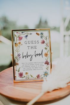 a sign that says guess the baby food on top of a wooden table with feathers