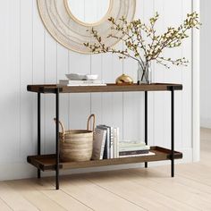 a console table with books, baskets and flowers in front of a white painted wall