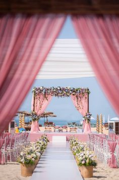 an outdoor ceremony set up with pink drapes and white flowers on the aisle to the beach