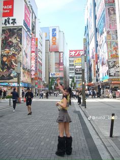 a woman standing in the middle of a city street waving to someone on her cell phone