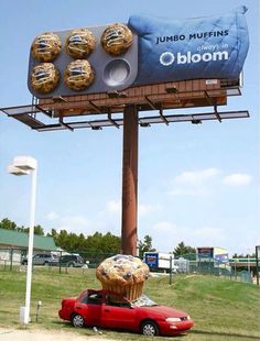 a billboard advertising muffins on top of a red car in front of a field