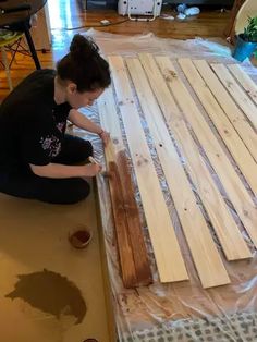 a woman sitting on top of a wooden floor next to a pile of wood planks