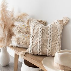 some pillows and hats are sitting on a wooden bench next to a white vase with flowers