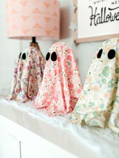 three little ghost figurines sitting on top of a white shelf next to a lamp