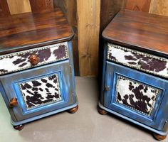 two blue and brown painted wooden nightstands with cow hide on the top, side by side