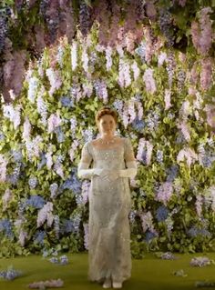 a woman standing in front of a flower wall with purple and blue flowers on it