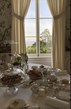 a table with plates and cups on it in front of a window