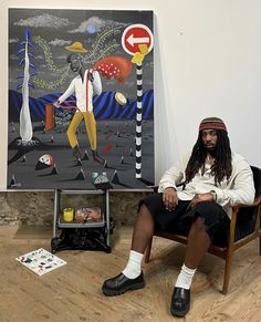 a man sitting in a chair next to a painting on the wall with other items around him