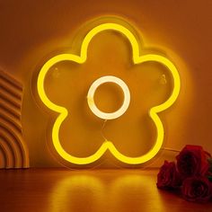 a flower shaped neon sign sitting on top of a table next to a red rose