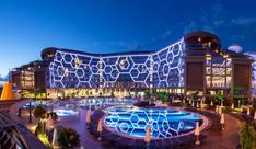 an outdoor swimming pool in front of a large building at night with lights on it