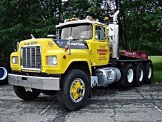 a large yellow truck parked on top of a parking lot next to some green trees