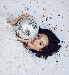 a woman laying on the floor with a disco ball in her hand and confetti all around her