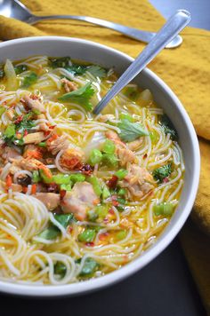 a white bowl filled with noodles, meat and veggies on top of a table