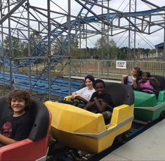 four people are riding on a roller coaster at an amusement park, with one person in the foreground smiling