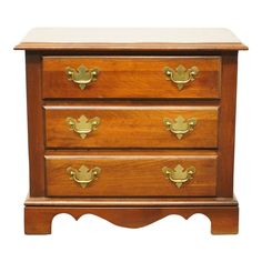 a wooden dresser with three drawers and brass pulls on the bottom drawer, against a white background