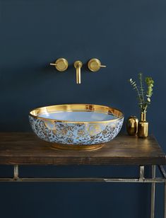 a gold and white bowl sink sitting on top of a wooden table next to a vase