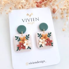 a pair of earrings with flowers on them sitting on top of a white card board