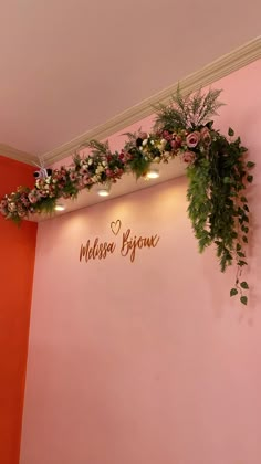 a pink wall with flowers and greenery hanging from it's sides in the corner