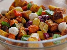 a glass bowl filled with colorful food on top of a wooden table next to a fork