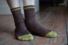 the legs of a person wearing brown socks with yellow stripes on them, standing on a wooden floor