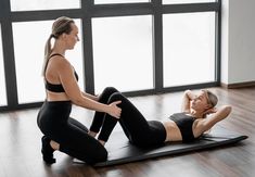 two women in black sports bras are doing exercises on a yoga mat while one woman is stretching her leg