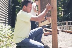 a man sitting on the ground working on a piece of wood that is attached to a fence