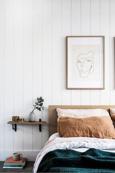 a bed with two pictures above it in a white room next to a wooden shelf