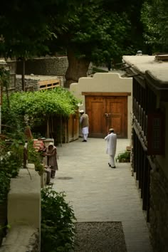 two men walking down a path in the middle of an alley way with trees on both sides