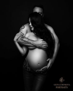 a black and white photo of a pregnant woman hugging her husband's belly with tattoos on their arms