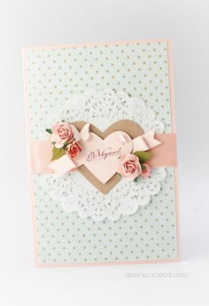 a heart shaped card with pink roses and lace on the edge, in front of a polka dot background