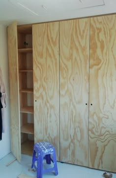 an unfinished closet with wooden walls and blue stools in the foreground, next to a white wall