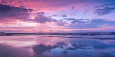 the sky is reflected in the wet sand on the beach as the sun goes down