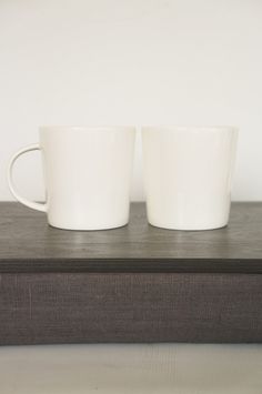 two white coffee mugs sitting on top of a wooden box next to each other