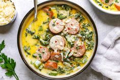 a bowl of soup with sausages, spinach and rice next to a spoon