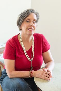 a woman sitting at a table wearing a red shirt and pearls on her necklaces