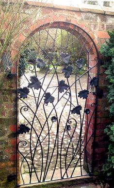 an iron gate with flowers on it in front of a brick wall and shrubbery