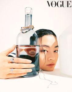 a woman holding a bottle with her face in it and another person's hand on top of the bottle