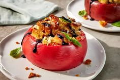 two red stuffed tomatoes on white plates with sauce drizzled over the top