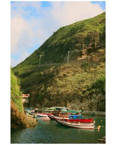 there are many boats that are docked on the water near some hills and cliffs with wind mills in the background