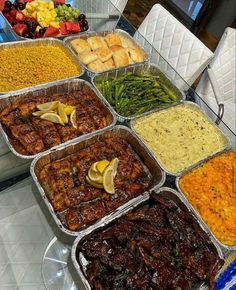 many trays of food are on display at a buffet table, including meat and vegetables