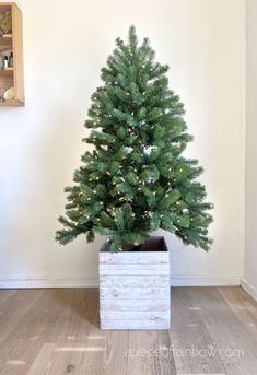 a small christmas tree sitting in a wooden box on the floor next to a wall