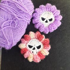 two crocheted flowers and a ball of yarn on a black surface with purple balls in the background