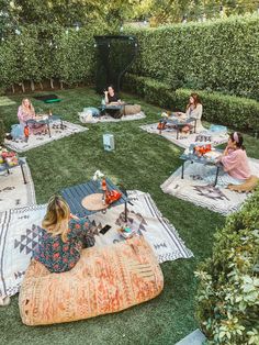 a group of people sitting on top of a lush green field next to trees and bushes